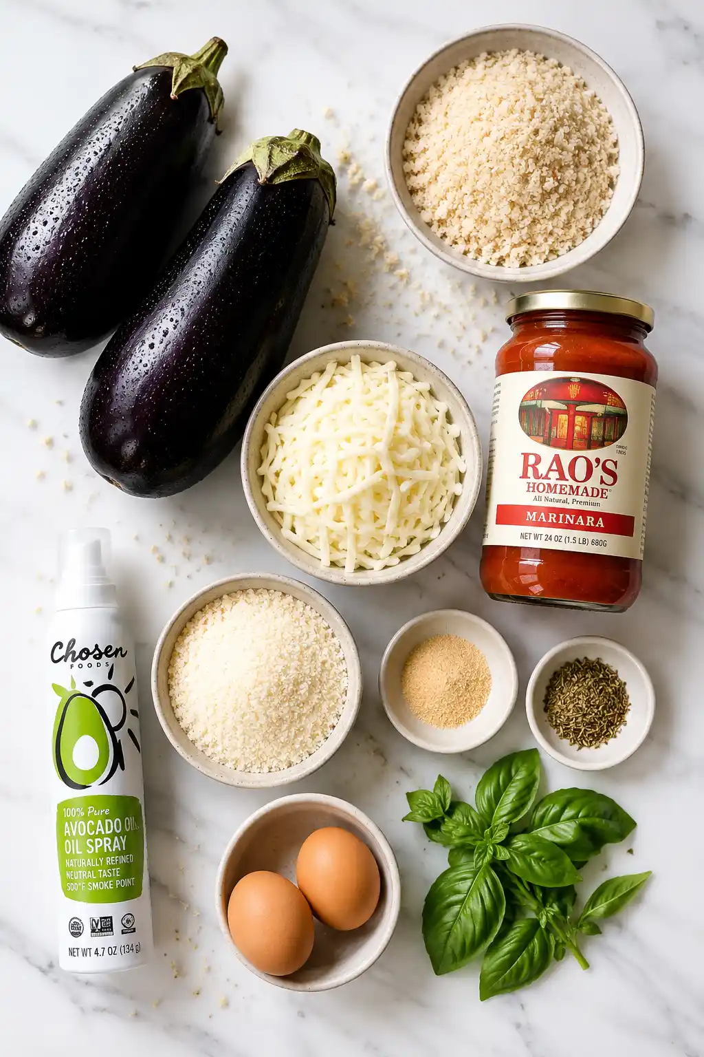 Flat lay of eggplant parmesan ingredients including fresh eggplants mozzarella parmesan breadcrumbs marinara sauce eggs and basil on marble background