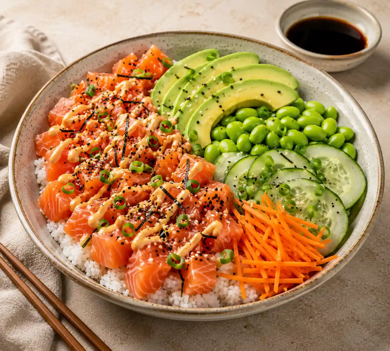 Salmon Sushi Bowl served with fresh salmon cubes over sushi rice, creamy avocado slices, edamame, cucumber, shredded carrots, green onions, sesame seeds, nori strips, and a drizzle of spicy mayo.