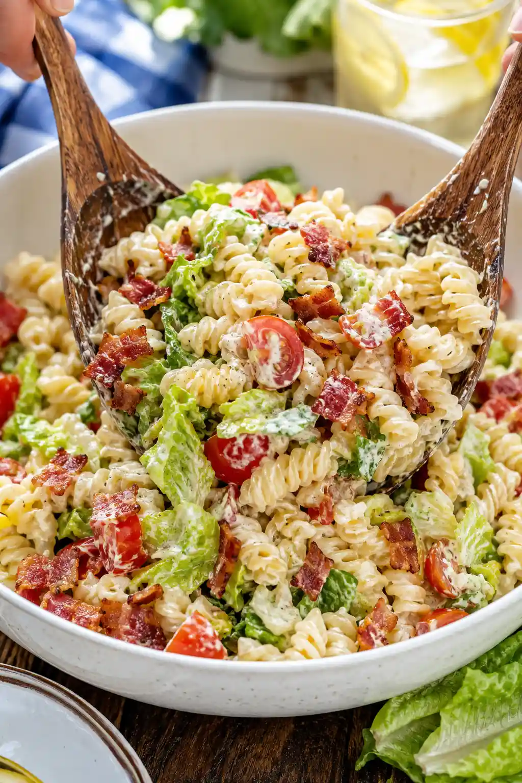 BLT pasta salad being tossed with crispy bacon cherry tomatoes romaine lettuce and creamy dressing