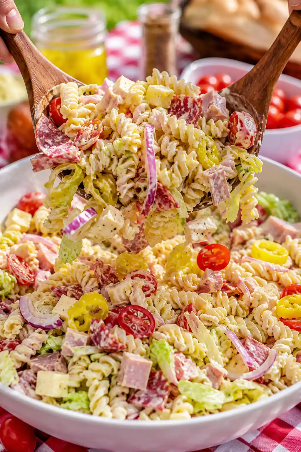 Grinder pasta salad being mixed with deli meats cheese lettuce tomatoes banana peppers and creamy dressing