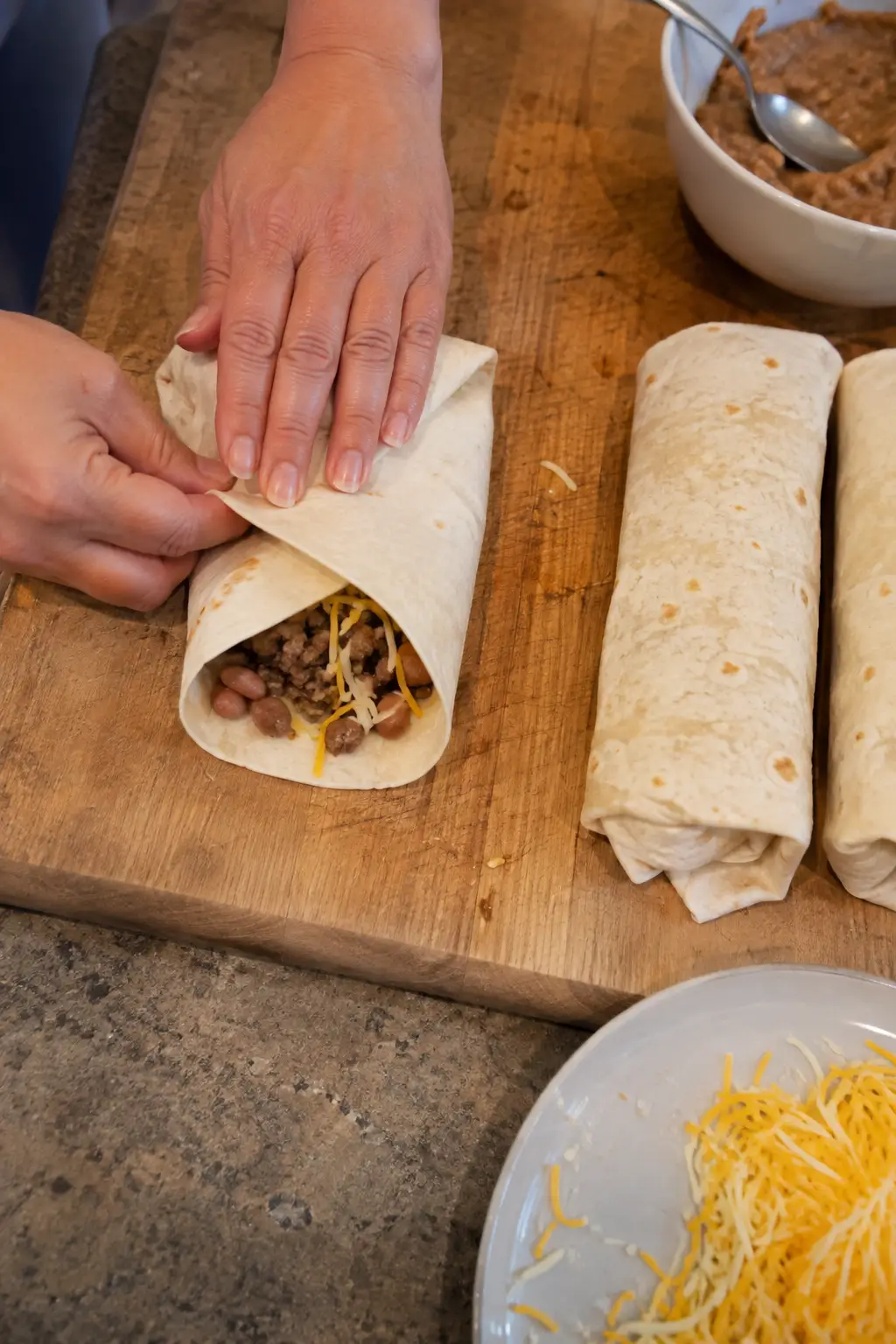 Tortilla being rolled around beef filling and shredded cheese
