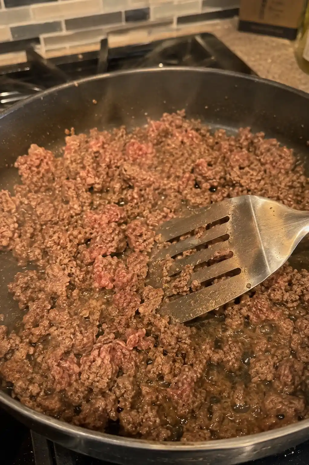 Ground beef browning in a skillet being broken apart with a spatula for sloppy joes