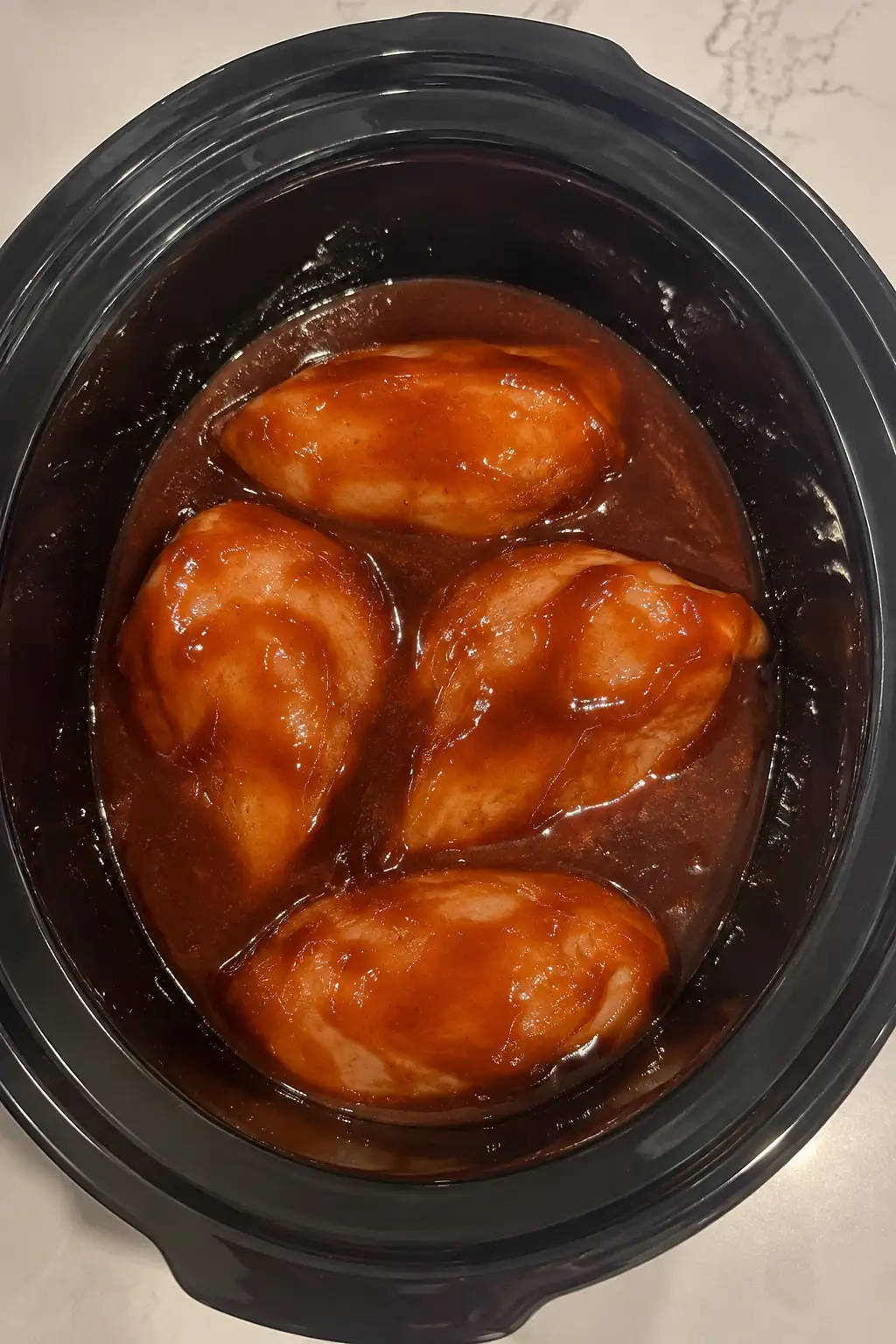 Raw chicken breasts coated in barbecue sauce inside a slow cooker