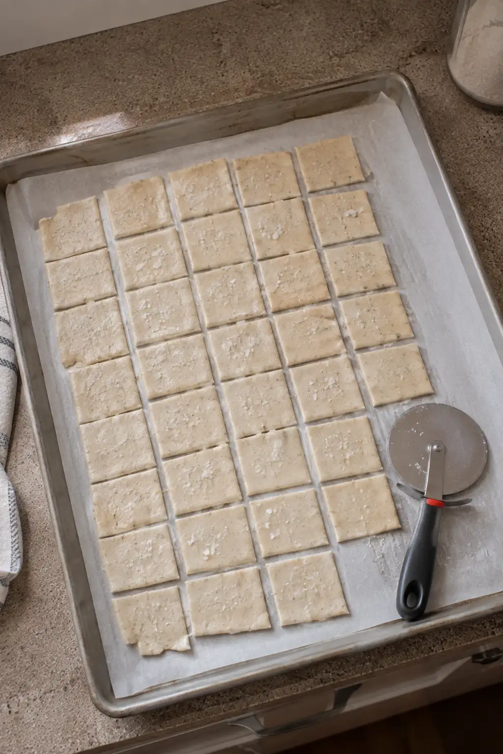 Thin sourdough cracker dough cut into small squares on a baking sheet
