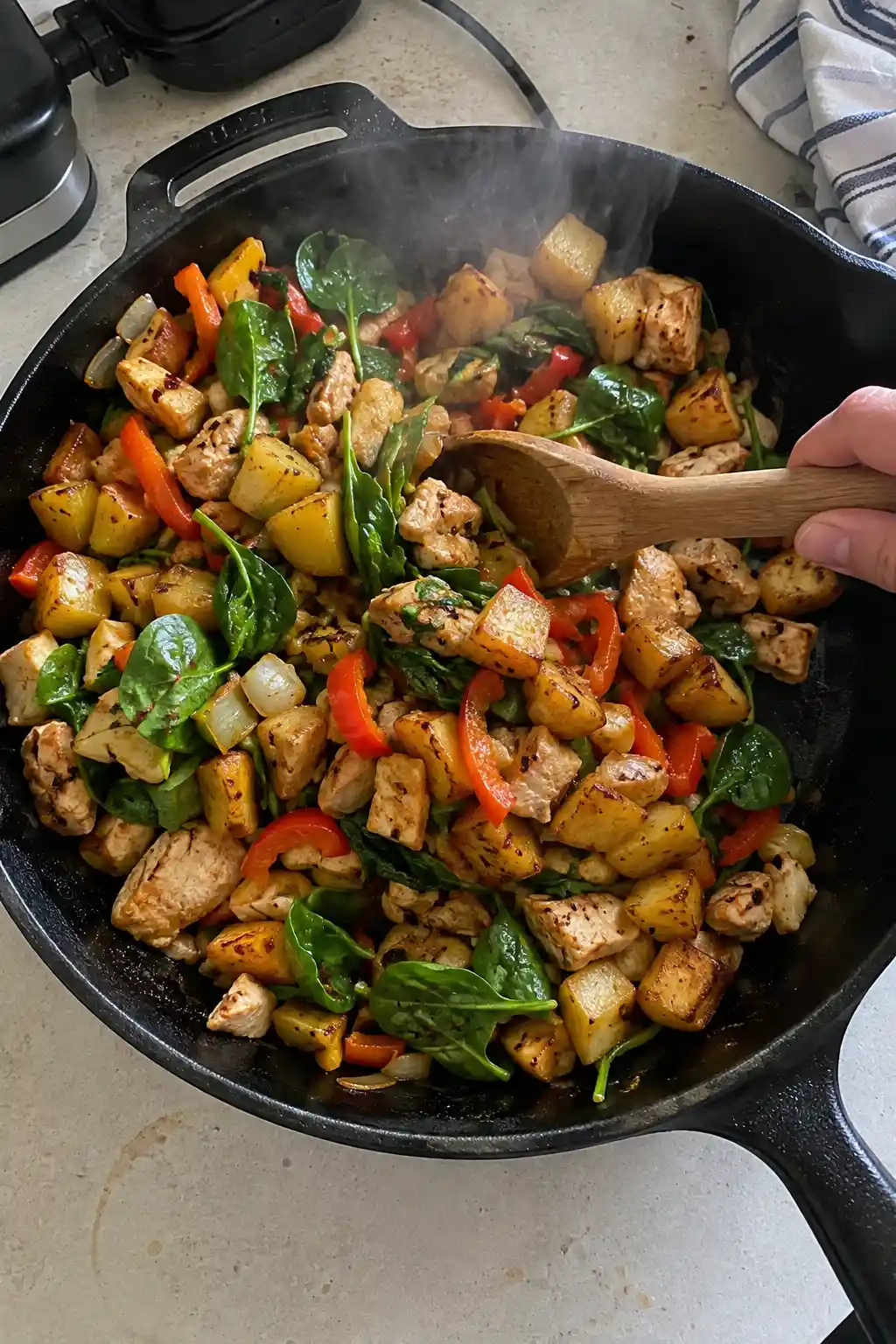 Skillet of crispy potatoes, chicken, vegetables, and spinach being stirred together