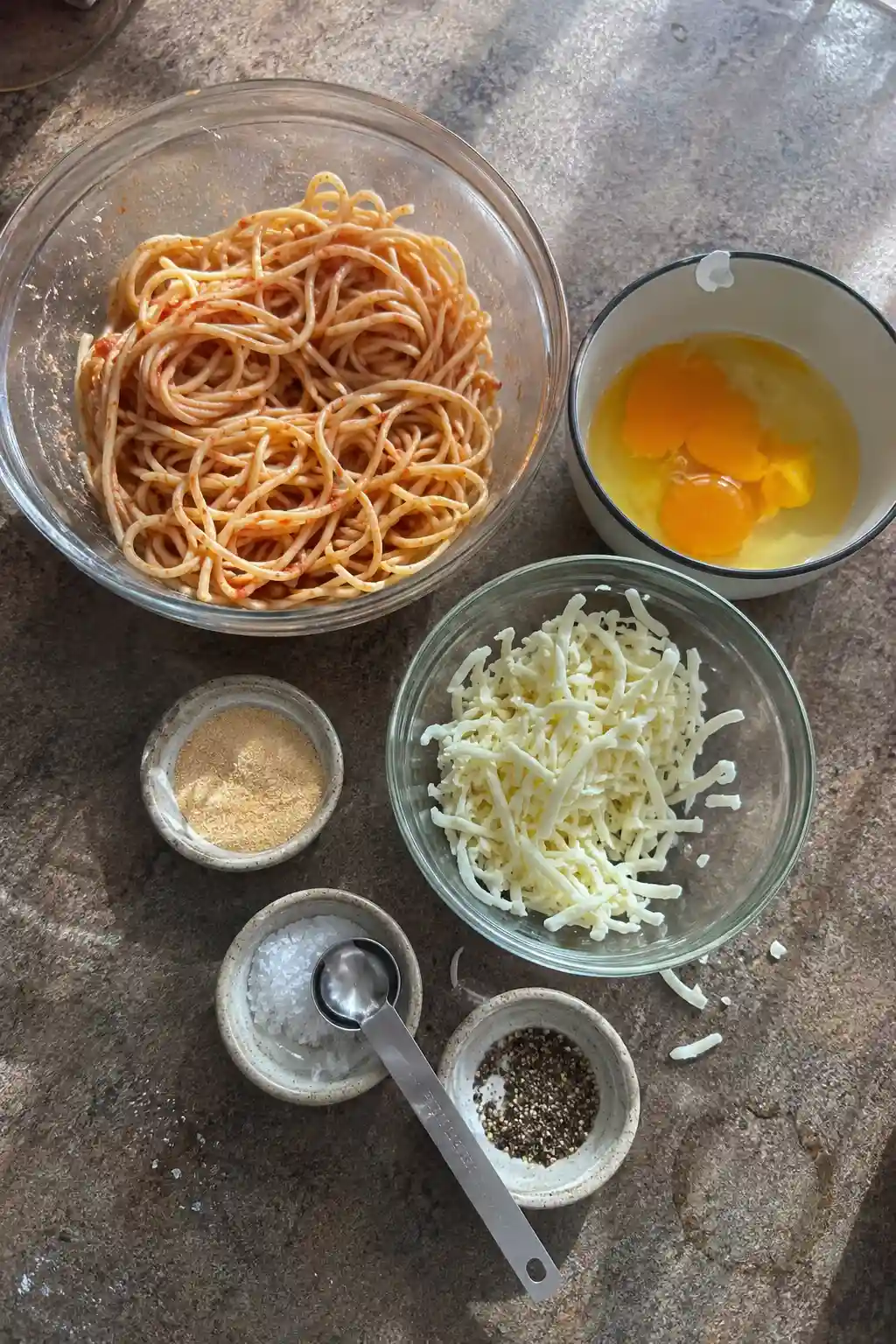 Ingredients for spaghetti cakes including leftover spaghetti, eggs, and shredded cheese