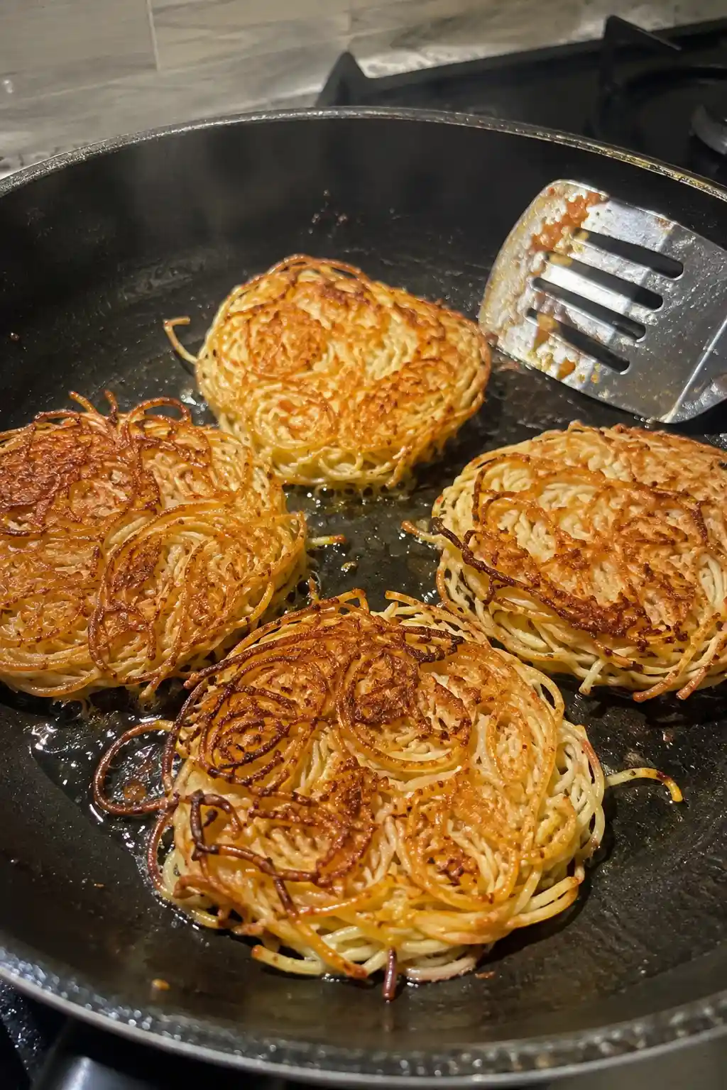 Spaghetti cakes frying golden brown in a skillet with crispy edges