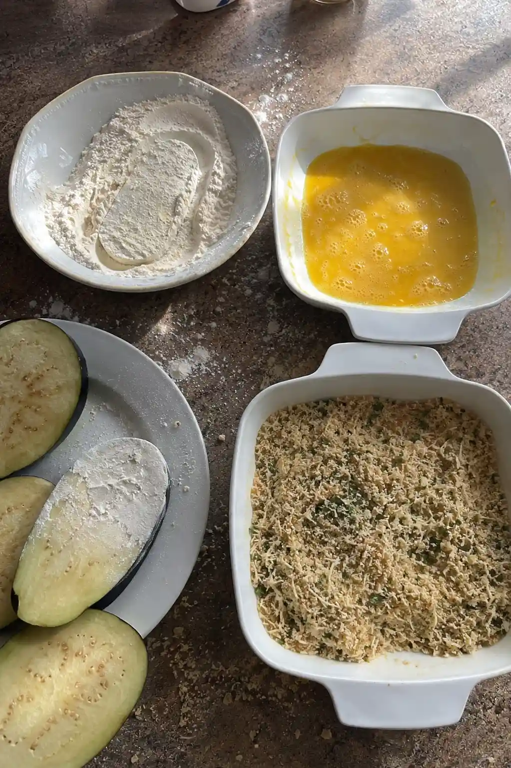 Breading station with flour, egg, and seasoned breadcrumbs for eggplant parmesan