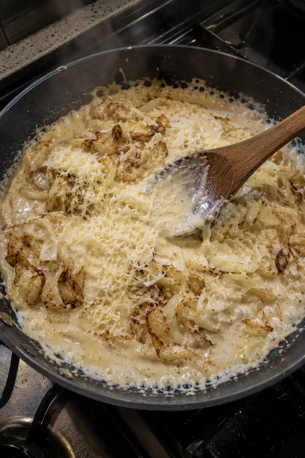 Caramelized cabbage and creamy alfredo sauce being stirred together in a skillet