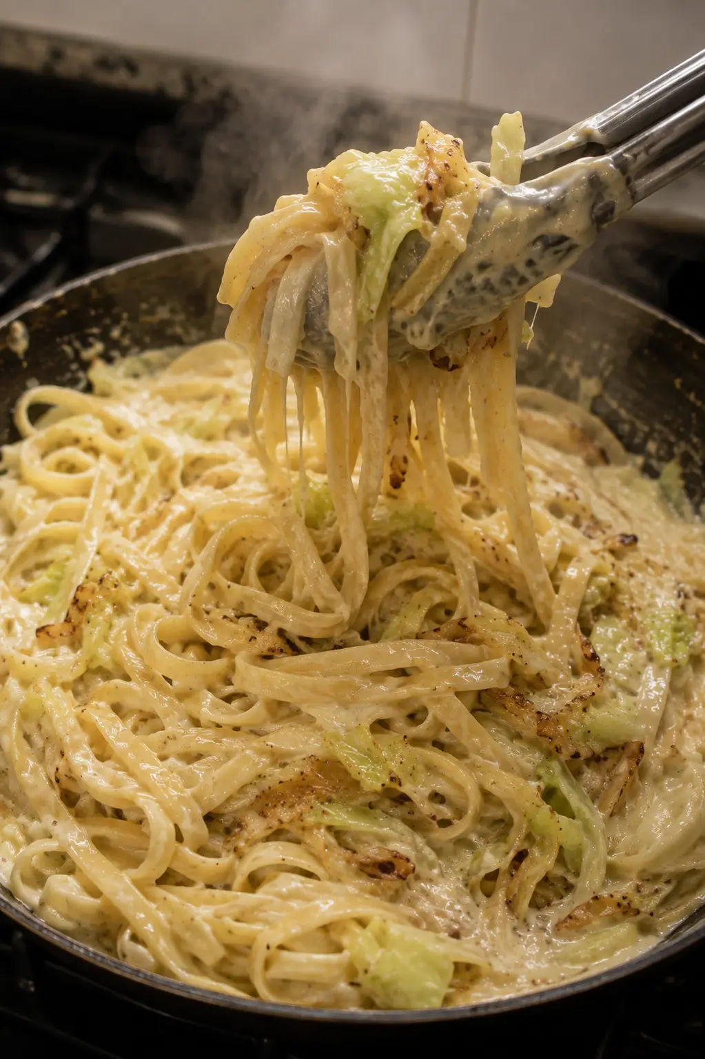 Fettuccine being tossed with cabbage alfredo sauce in a skillet