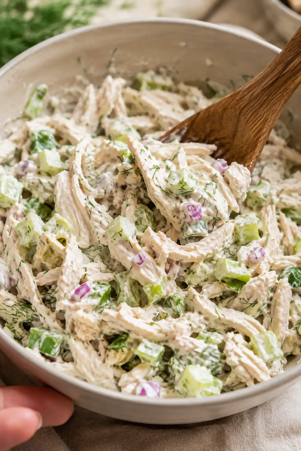 Shredded chicken and Greek yogurt dressing being stirred together with celery and herbs