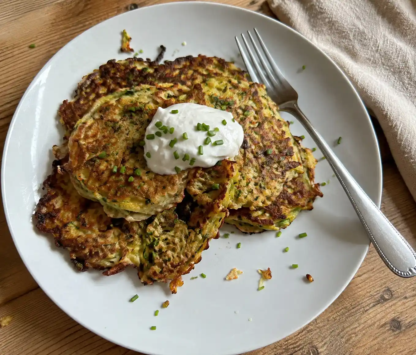 Stack of crispy golden zucchini fritters Recipe topped with sour cream and chives
