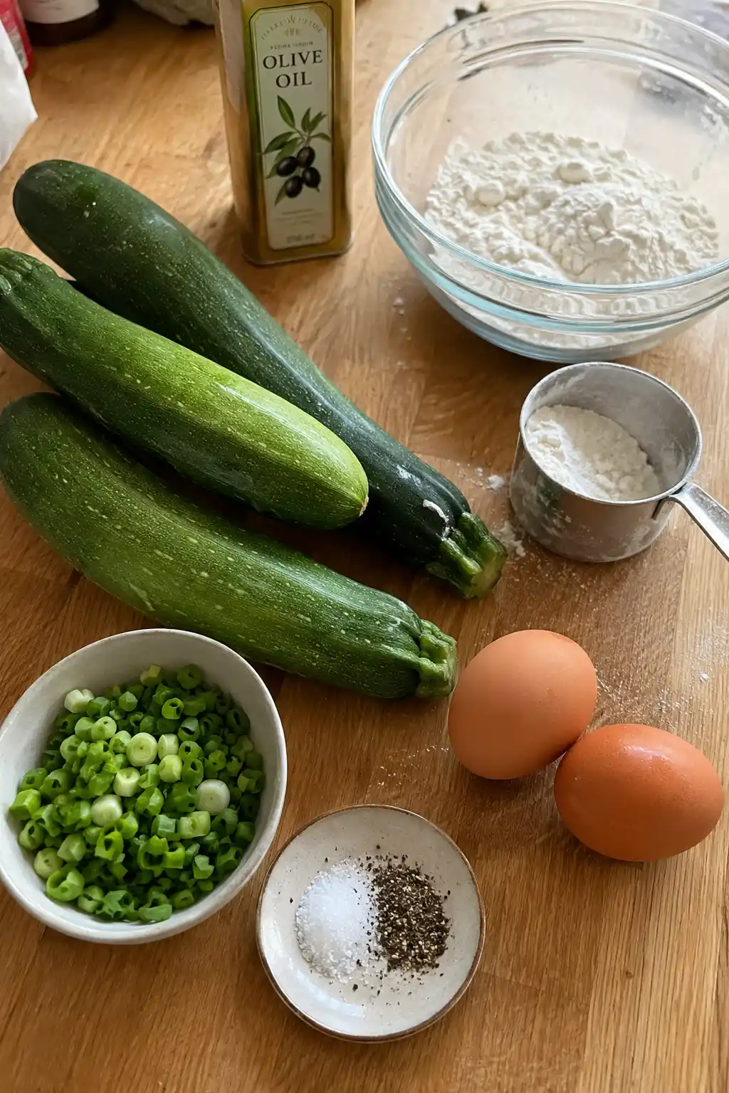 Ingredients for zucchini fritters including zucchini, green onion, eggs, and flour