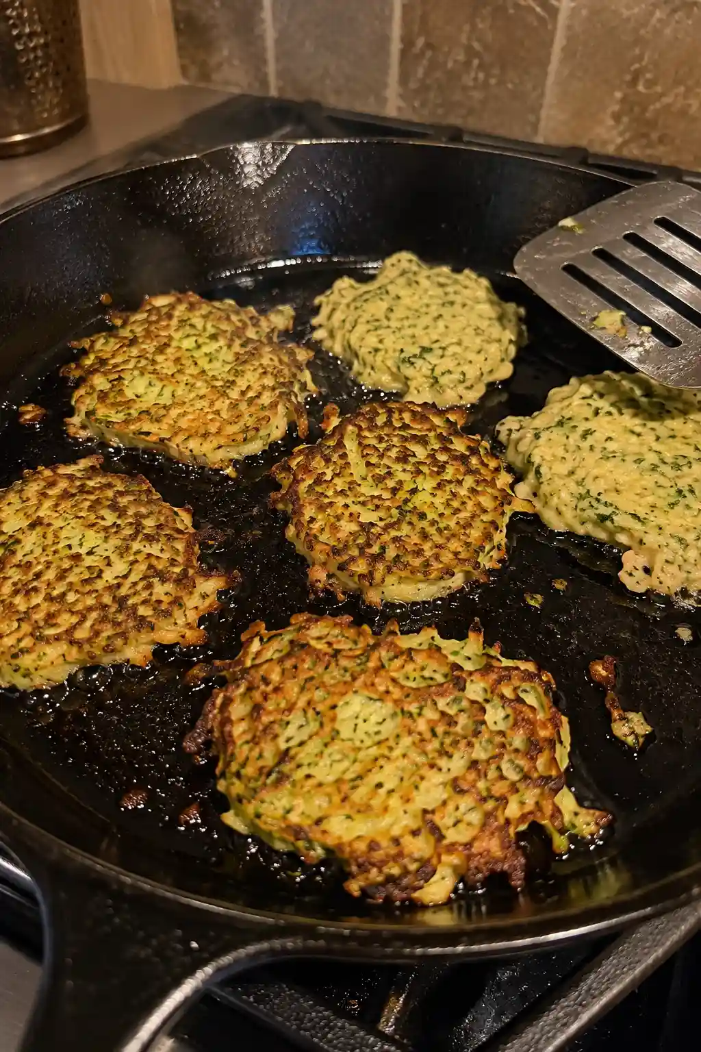 Zucchini fritters cooking and turning golden brown in a cast iron skillet