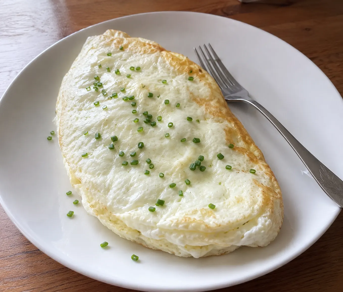 Folded fluffy egg white omelette on a white plate garnished with fresh chives