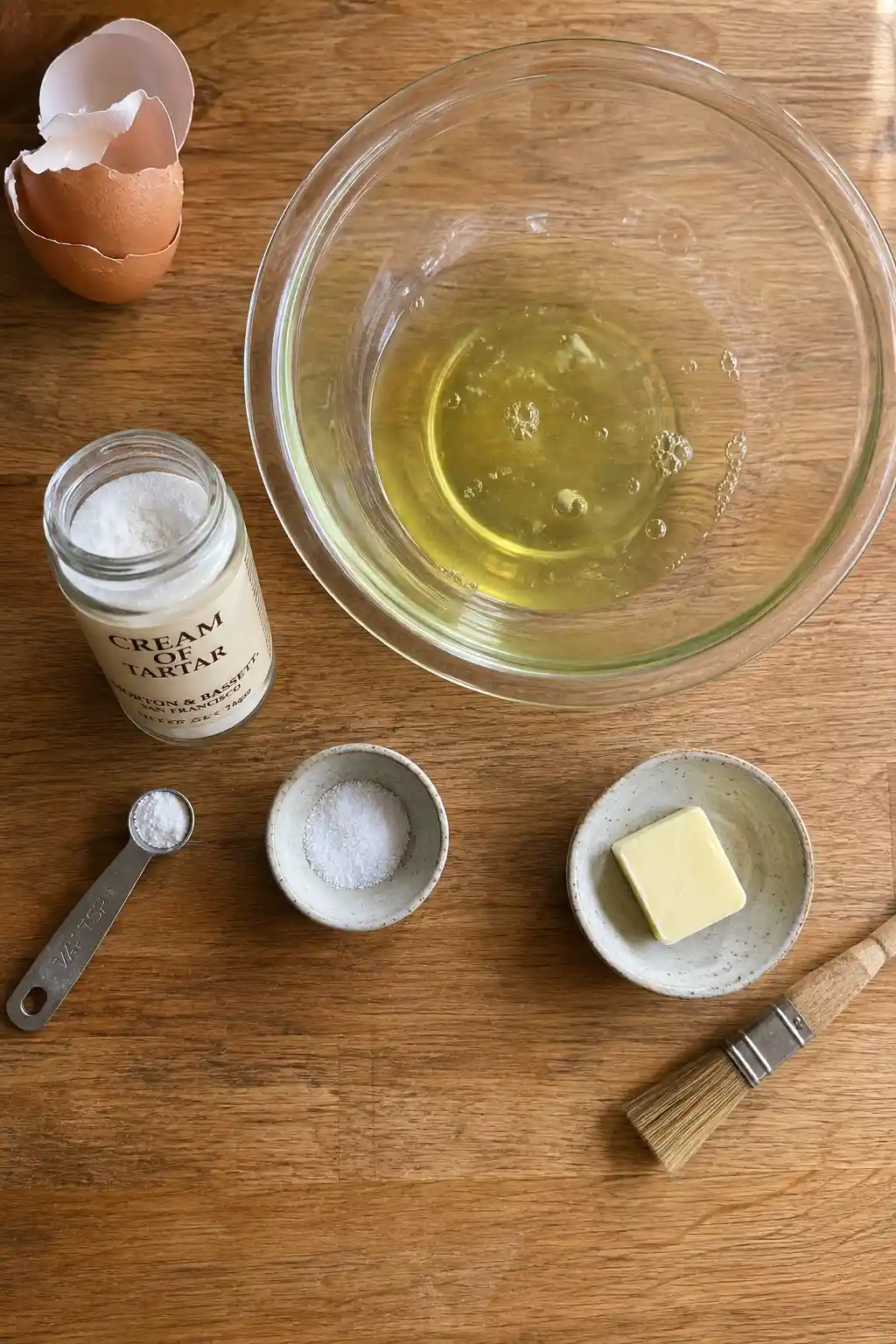 Egg whites in a glass bowl next to cream of tartar, salt, and butter for omelette recipe